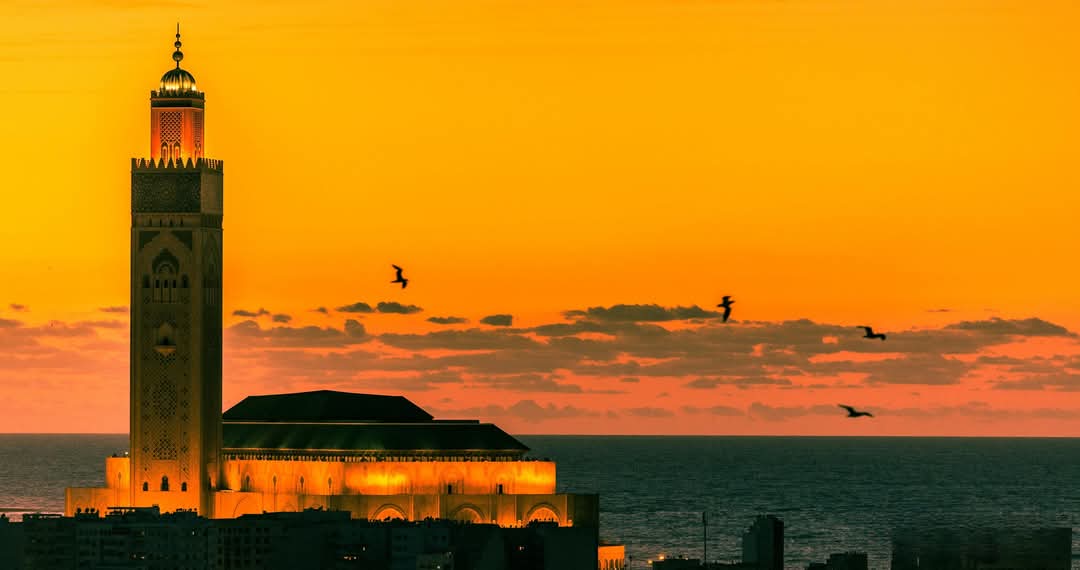 Hassan II Mosque along Casablanca waterfront with tall minaret rising above the Atlantic Ocean in warm evening light
